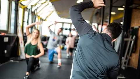 Instruktor fitness pokazuje ćwiczenia rozciągające grupie na siłowni